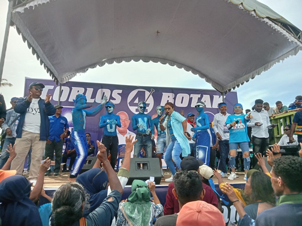 Penyanyi Lembata bernyanyi dan berjoget di atas panggung kampanye akbar Paket Tunas ditemani para pemilih pemula yang mengecat tubuh mereka dengan warna Biru dan bertulis TUNAS.