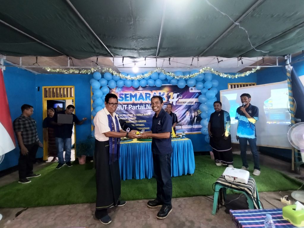 Ketua Dewan Pakar DPD Partai NasDem Lembata Mikael menyerahkan potongan tumpeng kepada mantan ketua DPD Partai NasDem Hendrik Mosa Langobelen pada puncak perayaan HUT ke-14 Partai NasDem, Selasa, 11 November 2025.